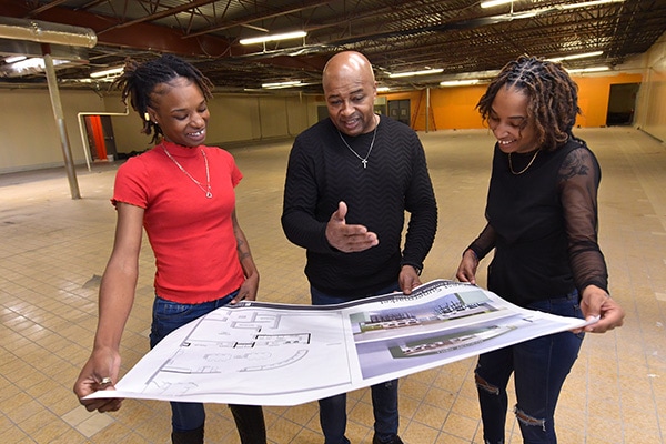 People standing in an old empty store with building plans