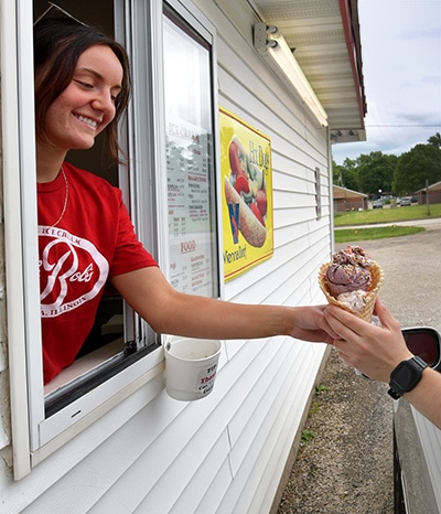 Woman hands an ice cream cone to a customer in the drive thru
