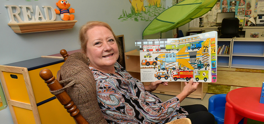 A Woman sitting in a rocking chair holding a children's picture book