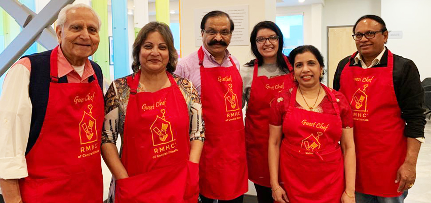 A group of people in Red aprons|Dr. Kiran Velpula is sworn in at Peoria City Hall|Men holding a large check for St Jude|Women shopping in food market