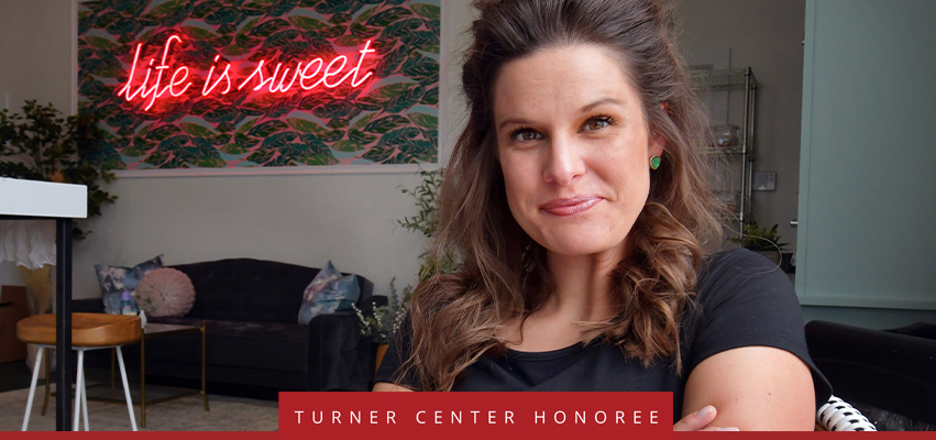 Turner Center Nominee: A woman istting in a living space with a neon sign - "Life is sweet"