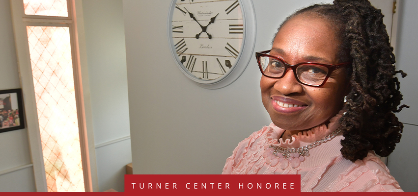 Turner Center Nominee: A woman looking at the camera standing in front of a wall and a clock.
