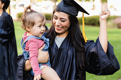 Woman in a graduation cap and gown holding an infant