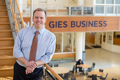 Man standing on stairs overlooking a common area with tables with a sign in the background "Geis Business"