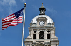 The Unit3ed States Flag and the Courthouse clock tower against a blue sky.