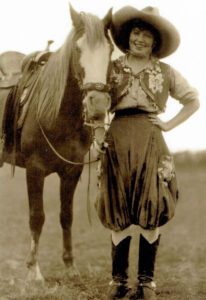 A vintage photo of a woman dressed as a cow girl standing with a horse