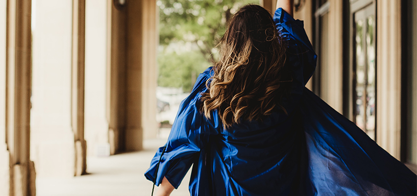 Woman in blue cap and gown Walking down an arched walkway