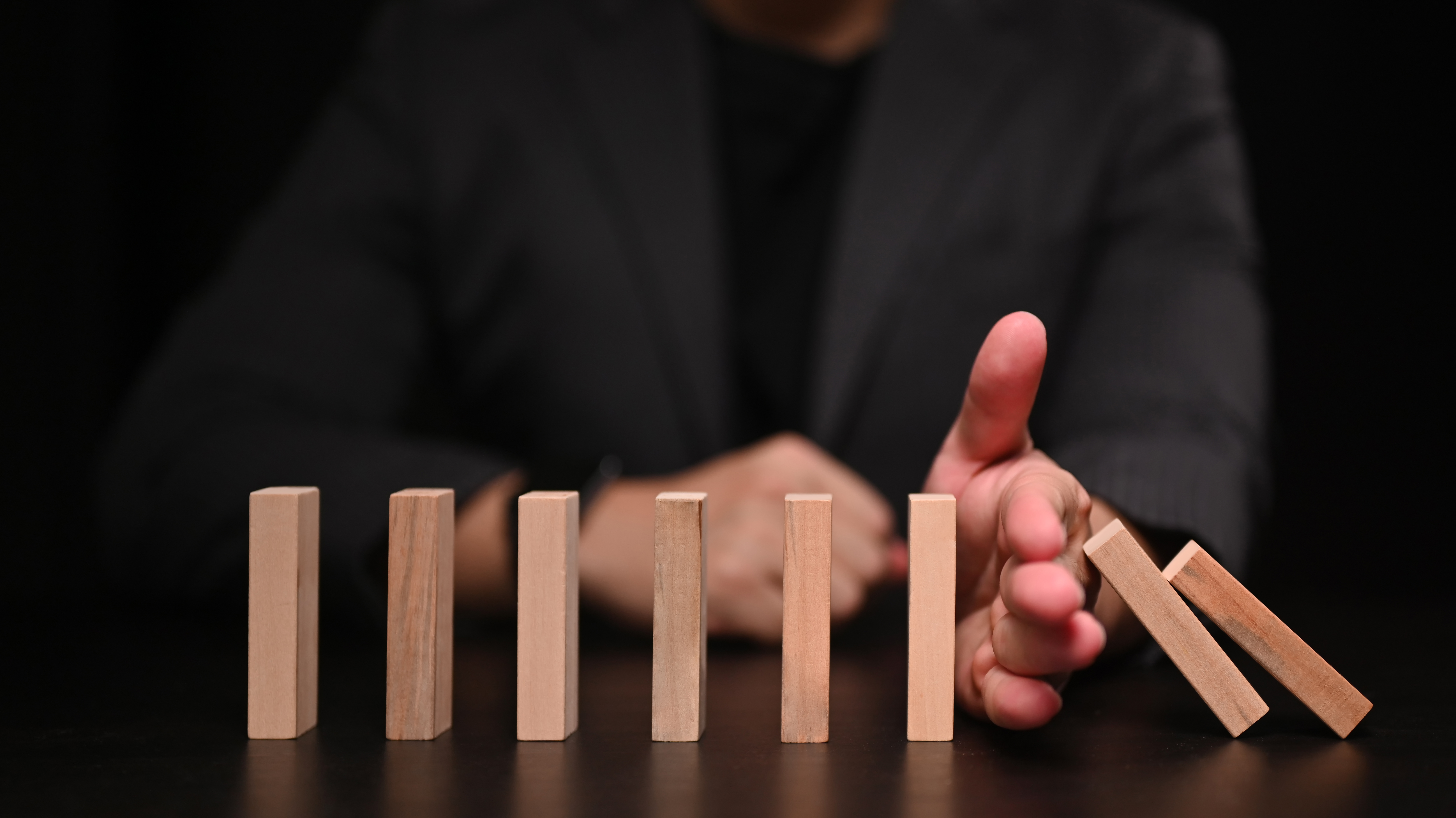 Businessman hand trying to stop dominoes. Protection finance from domino effect concept.