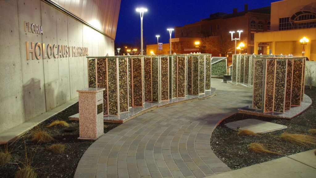The Peoria Holocaust Memorial after dark with lights illuminating the exhibit outside the Peoria Riverfront Museum